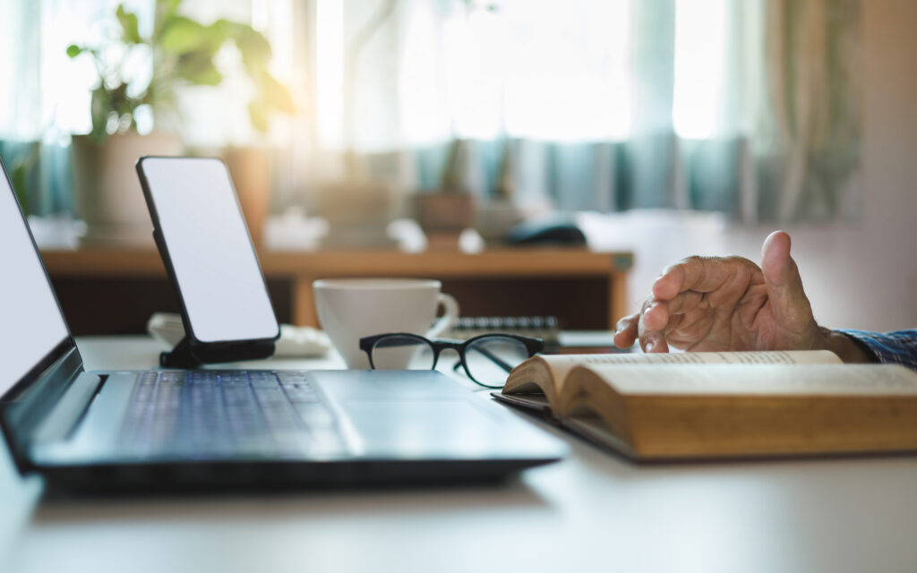 A desk with a laptop, smartphone, cup of coffee, glasses, and an open book